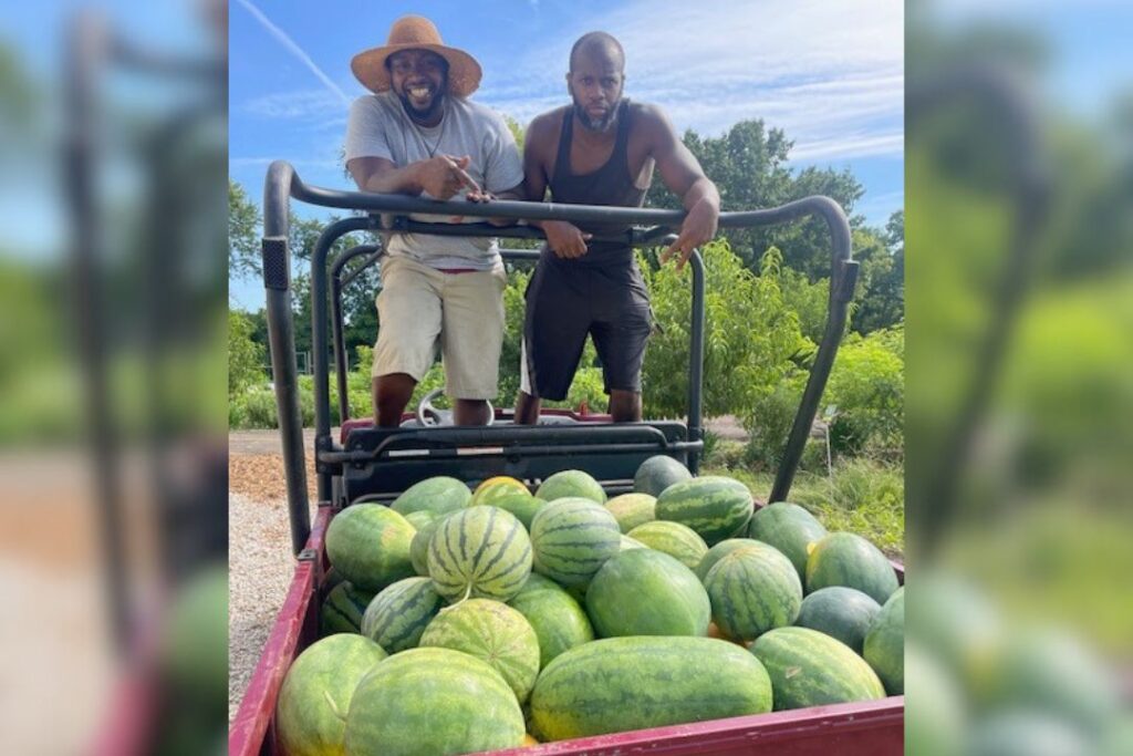 Tyrean "Heru" Lewis and a coworker pose for a photo next to a cart of watermelons.