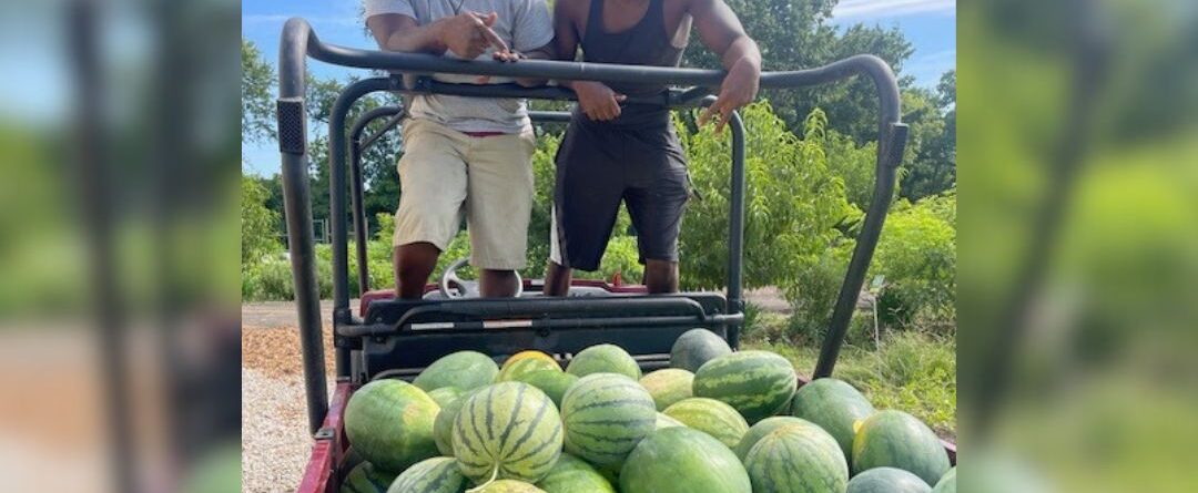 Tyrean "Heru" Lewis and a coworker pose for a photo next to a cart of watermelons.